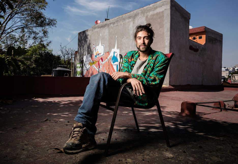 Angelo Barreto poses on a rooftop near one of his murals