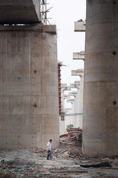 A man walks under new construction for an elevated roadway and high speed rail line in Hainancun, Liwan